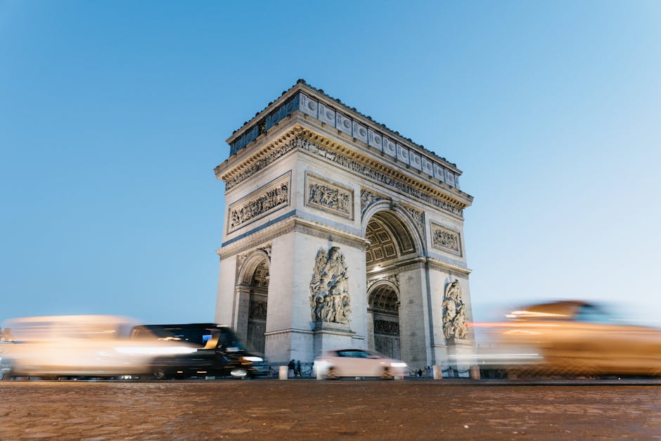 Arc de Triomphe in Paris at dusk with motion-blurred traffic passing by.